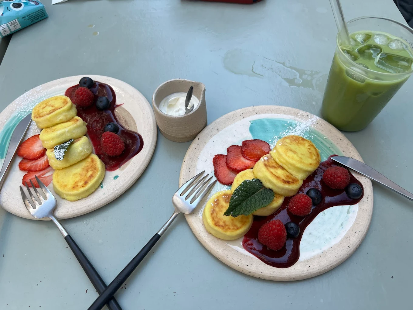 Deux assiettes de syrniki vues de dessus et un matcha latte glacé sur une table, chez Sublime Coffee à Genève.